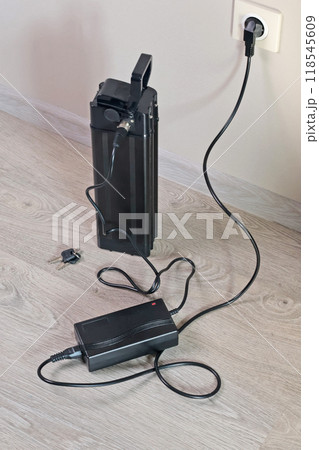 Charging bicycle battery from mains electricity in house. Socket in room with plug switched on. Environmentally friendly transport.  118545609