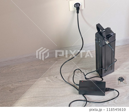 Charging bicycle battery from mains electricity in house. Socket in room with plug switched on. Environmentally friendly transport.  118545610