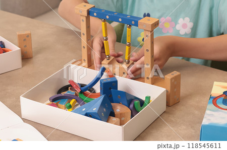Girl assembles swing from magnetic wooden construction set. Toys and activiti children. Developmental activities at home.  118545611