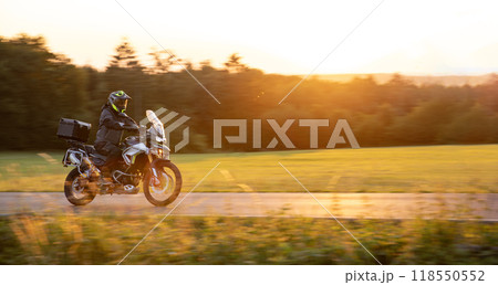 Driver riding motorcycle on empty road during sunset Driver riding motorcycle on empty road during sunset 118550552