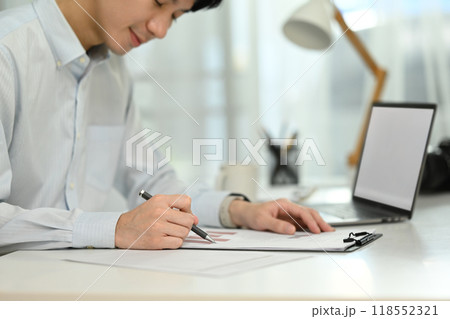 A man is writing on a piece of paper with a pen A man is writing on a piece of paper with a pen 118552321