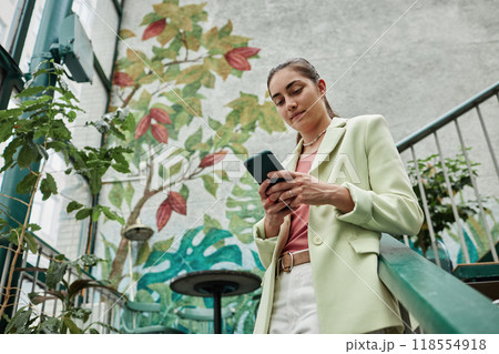 Low angle shot of Caucasian woman texting on social network while in eco cafe 118554918