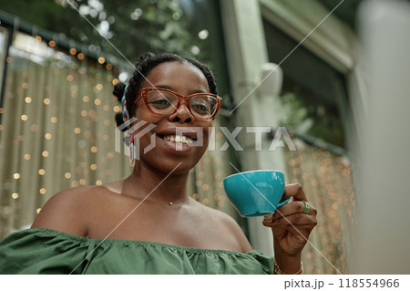 Low angle shot of happy African American woman holding turquoise ceramic cup full of herbal tea 118554966