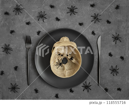 Halloween table setting with black dishes and skull on dark gray background with spiders. View from above. Halloween table setting with black dishes and skull on dark gray background with spiders. View from above. 118555716