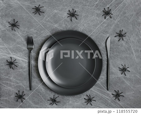Empty black plate with black cutlery on a gray background with cobwebs and spiders. Halloween table setting with copy space. Empty black plate with black cutlery on a gray background with cobwebs and spiders. Halloween table setting with copy space. 118555720