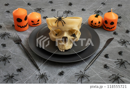 Halloween festive table setting with skull and candles on gray background with cobwebs and spiders. Serving for Halloween party. Halloween festive table setting with skull and candles on gray background with cobwebs and spiders. Serving for Halloween party. 118555721
