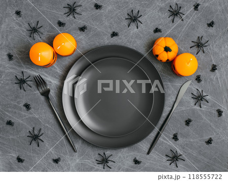 Halloween table setting with black dishes, orange candles, cobwebs and spiders on gray background. Copy space, top view, flat lay. 118555722