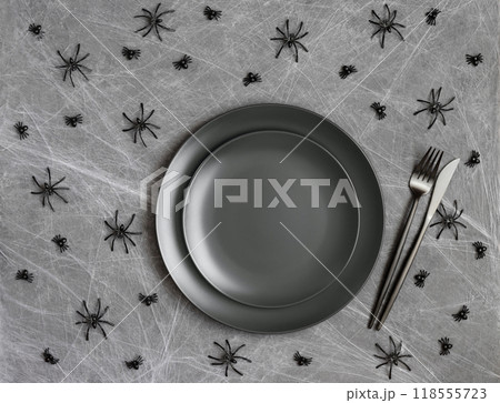 Halloween table setting with black cutlery and spiders on dark gray background with cobweb. Serving with empty black plate for design. Mockup or template. 118555723