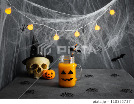 Festive Halloween drink decorated with creepy cobwebs, skulls and spiders on gray background. Halloween cocktail with spooky smile in a glass jar. Copy space. Festive Halloween drink decorated with creepy cobwebs, skulls and spiders on gray background. Halloween cocktail with spooky smile in a glass jar. Copy space. 118555737