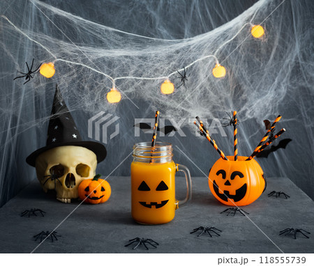 Halloween decorations for party with drinks. Cocktail in a glass jar with creepy smile, drinking straws and skull on blue background. Halloween decorations for party with drinks. Cocktail in a glass jar with creepy smile, drinking straws and skull on blue background. 118555739