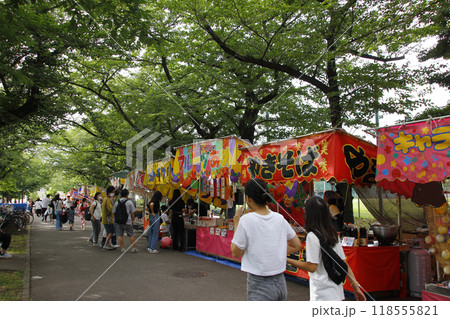 縁日の露店は桜並木の木々の下の木漏れ日の中で、思い思いに食べ歩いて祭りを楽しむ 縁日の露店は桜並木の木々の下の木漏れ日の中で、思い思いに食べ歩いて祭りを楽しむ 118555821
