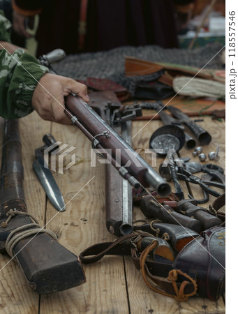 Set of antique firearms, bayonets, saber and peak tips on wooden table. Human hand holds a rifle, selective focus. 118557546