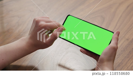Young woman sitting at a table and using a smartphone with horizontal green screen Young woman sitting at a table and using a smartphone with horizontal green screen 118558680