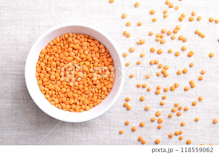 Red lentils in a white bowl on linen. Lentil variety with husk removed for a shorter cooking time and to avoid soaking. Dried fruits of Lens culinaris, an edible legume with lens-shaped seeds. Photo Red lentils in a white bowl on linen. Lentil variety with husk removed for a shorter cooking time and to avoid soaking. Dried fruits of Lens culinaris, an edible legume with lens-shaped seeds. Photo 118559062