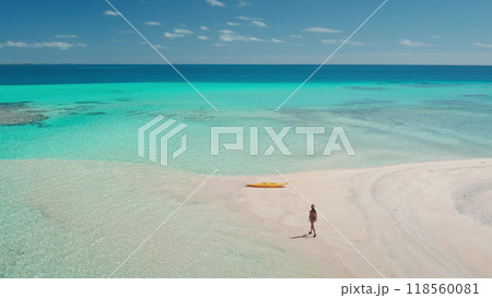 Aerial drone view of a woman walking on a pristine white sand beach towards crystal clear turquoise water with a yellow kayak, creating a sense of wanderlust and tropical paradise Aerial drone view of a woman walking on a pristine white sand beach towards crystal clear turquoise water with a yellow kayak, creating a sense of wanderlust and tropical paradise 118560081