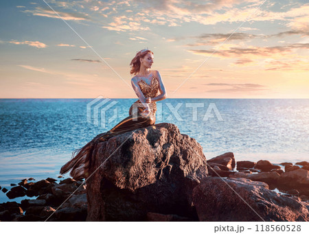 Sadness mermaid, nixie, water nymph sitting on stone. Sea, sunset view 118560528