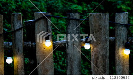 Small light bulbs decorated along a rustic wooden fence in a local restaurant, casting a warm, cozy glow. The soft lighting enhances the inviting atmosphere, creating a relaxed and intimate dining 118560632