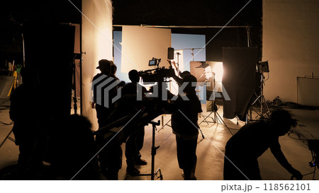 Silhouette of film crews and video camera on special dolly crane with film lights equipment and blue screen set. Film Production behind the scenes studio set in silhouette style. Behind video shooting Silhouette of film crews and video camera on special dolly crane with film lights equipment and blue screen set. Film Production behind the scenes studio set in silhouette style. Behind video shooting 118562101