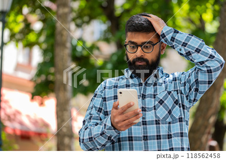 Surprised Indian man use smartphone loses, bad news, fortune loss, fail outdoors in city street 118562458