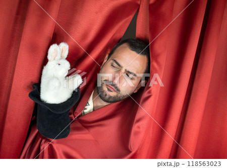 Funny young adult man magician with interesting face playing with rabbit out hat 118563023