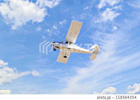 Single engine ultralight plane flying in the blue sky with white clouds Single engine ultralight plane flying in the blue sky with white clouds 118564354