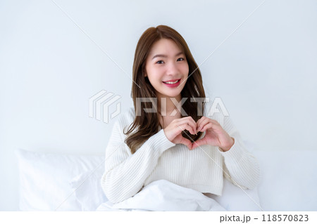 Front view of cute young Asian woman smiling and looking at camera with hands showing heart shape Front view of cute young Asian woman smiling and looking at camera with hands showing heart shape 118570823