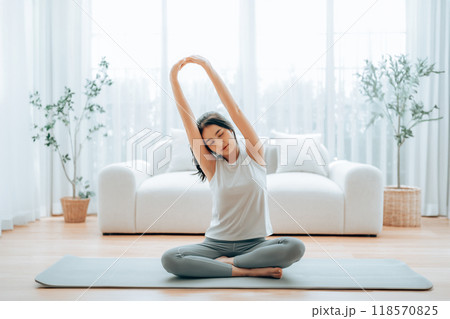 Happy young Asian woman practicing yoga and shoulder stretching at home 118570825