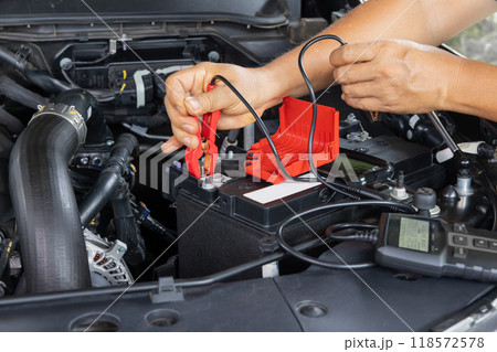 Man is measuring AGM battery power of suv car by battery tester at home. 118572578