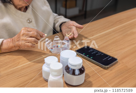Elderly woman putting pills into pill box for the week. Elderly woman putting pills into pill box for the week. 118572589