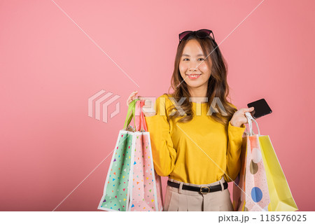 Portrait Asian happy beautiful young woman teen shopper smiling standing excited holding online shopping bags online colorful on mobile phone or smartphone studio shot isolated on pink background Portrait Asian happy beautiful young woman teen shopper smiling standing excited holding online shopping bags online colorful on mobile phone or smartphone studio shot isolated on pink background 118576025