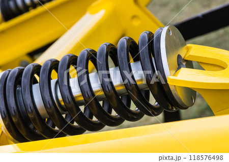 Steel black spring as part of yellow agricultural machine. Technology 118576498