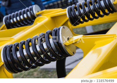 Steel black spring as part of yellow agricultural machine. Technology 118576499