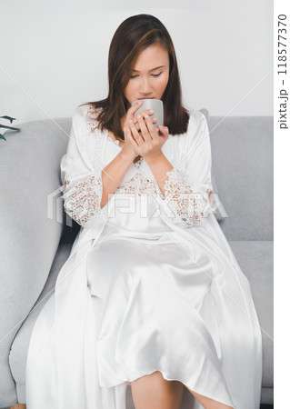 An Asian woman enjoys a hot drink of tea at night. 118577370