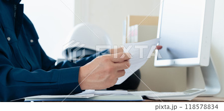 パソコンと資料を見比べる作業着の男性 パソコンと資料を見比べる作業着の男性 118578834