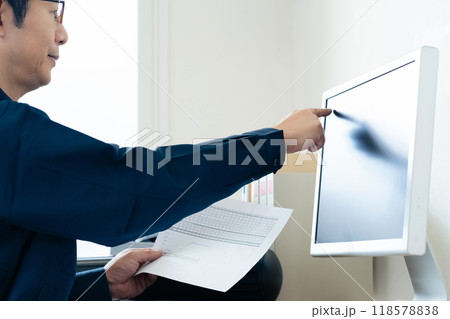 パソコンと資料を見比べる作業着の男性 118578838