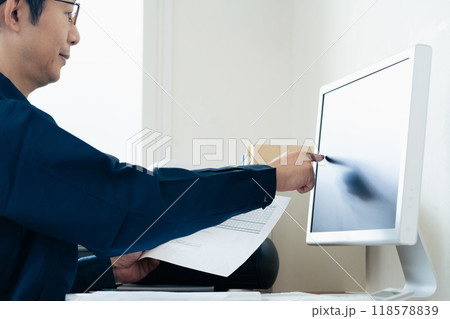 パソコンと資料を見比べる作業着の男性 118578839