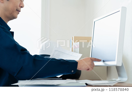 パソコンと資料を見比べる作業着の男性 118578840