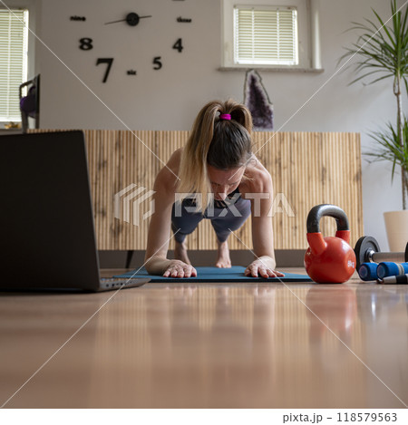 Front view of a young fit woman exercising with laptop computer in front of her via online course Front view of a young fit woman exercising with laptop computer in front of her via online course 118579563
