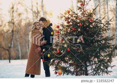 Young adult couple man and woman decorates pine tree in winter park forest. New year tree holiday party celebration concept Young adult couple man and woman decorates pine tree in winter park forest. New year tree holiday party celebration concept 118582247