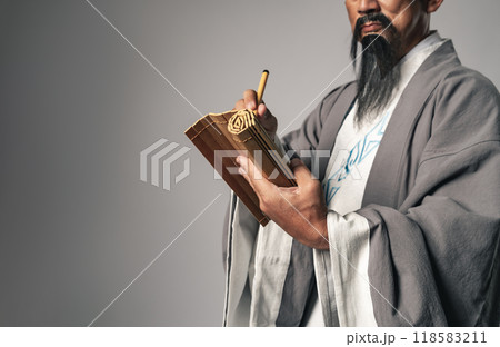 三国志に登場する諸葛孔明のような中国歴史上の人物が竹簡に毛筆で文字を書くシーン 118583211