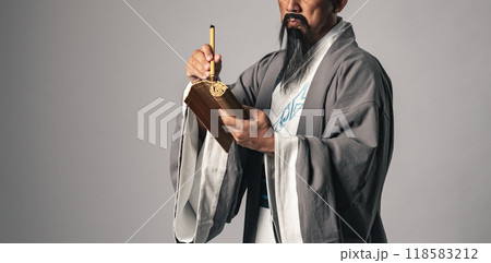三国志に登場する諸葛孔明のような中国歴史上の人物が竹簡に毛筆で文字を書くシーン 118583212