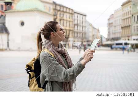 Attractive young female tourist is exploring new city. Happy girl holding a paper map on Market Square in Krakow. Traveling Europe in autumn. Attractive young female tourist is exploring new city. Happy girl holding a paper map on Market Square in Krakow. Traveling Europe in autumn. 118583591