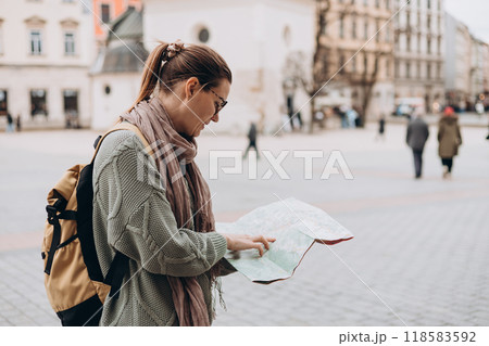 Attractive young female tourist is exploring new city. Happy girl holding a paper map on Market Square in Krakow. Traveling Europe in autumn. Attractive young female tourist is exploring new city. Happy girl holding a paper map on Market Square in Krakow. Traveling Europe in autumn. 118583592