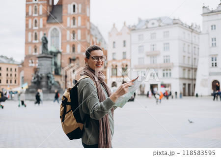 Attractive young female tourist is exploring new city. Happy girl holding a paper map on Market Square in Krakow. Traveling Europe in autumn. St. Marys Basilica 118583595
