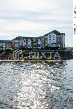 明るい日差しがキラキラ反射する海面と海岸脇に立つレンガ造りのアパート 南ウェールズの郊外にて 明るい日差しがキラキラ反射する海面と海岸脇に立つレンガ造りのアパート 南ウェールズの郊外にて 118584620