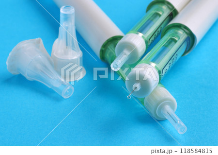 Insulin syringe pens and insulin needles with a drop of medicine at the needle tip isolated on a blue background Insulin syringe pens and insulin needles with a drop of medicine at the needle tip isolated on a blue background 118584815