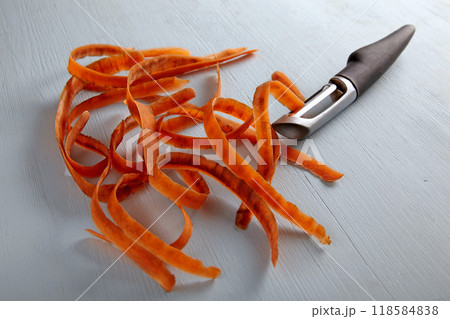 Carrot peelings and black metal peeler on a light wooden table 118584838