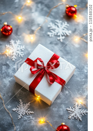 Festively wrapped Christmas gift with red ribbon and decorations on a textured grey background 118588102