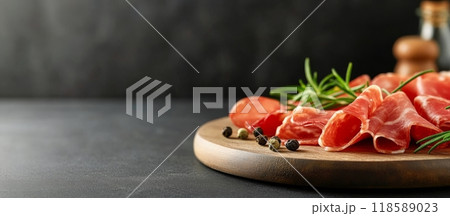 Slices of cured meat arranged on a wooden board with herbs and spices in a dark setting 118589023