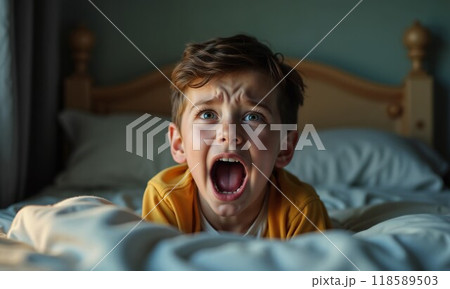 A boy lies on a bed, mouth open, making a funny face 118589503
